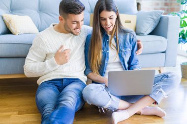 Genç çift bilgisayar laptop kullanarak yeni ev katında oturan ve yeni bir eve taşımak için mutlu gülümseyen