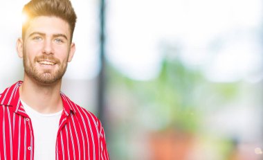 Hayret ve el ile sunulması ve parmak ile işaret ederken kameraya gülümseyen kırmızı gömlek giymiş genç yakışıklı adam.