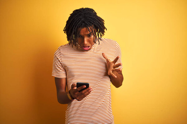 Afro american man with dreadlocks using smartphone over isolated yellow background very happy and excited, winner expression celebrating victory screaming with big smile and raised hands