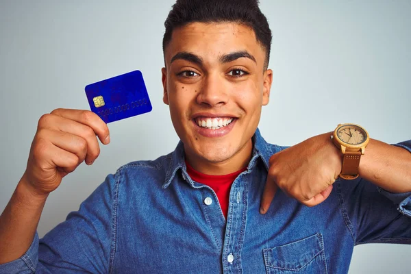 年轻的巴西客户男子拿着信用卡站在孤立的白色背景与惊喜的脸指向自己 — 图库照片