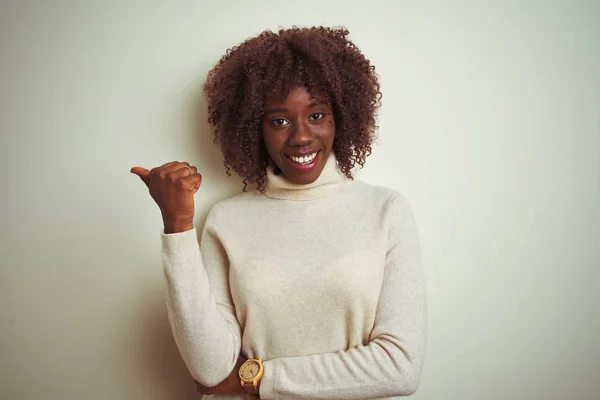 孤立した白い背景の上にタートルネックのセーターを着た若いアフリカのアフロ女性は 幸せそうな顔で微笑み 親指を上げて側面を指差す — ストック写真