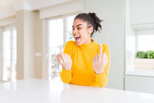 Beautiful african american woman with afro hair wearing a casual yellow sweater Showing middle finger doing fuck you bad expression, provocation and rude attitude. Screaming excited