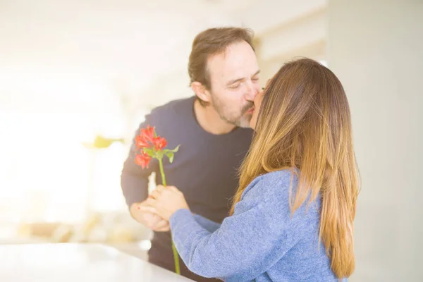 Romántica pareja de mediana edad sosteniendo flores besándose en el amor en ho — Foto de Stock