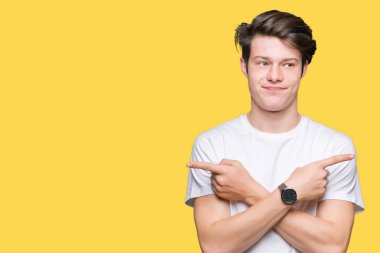 Genç yakışıklı adam giyiyor rahat beyaz t-shirt üzerine izole arka plan için her iki parmak, farklı yönde ile katılmıyorum işaretleme