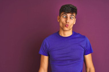 Genç hint adam izole mor arka plan üzerinde duran t-shirt giyen dudakları ile balık yüz yapma, deli ve komik jest. Komik ifade.