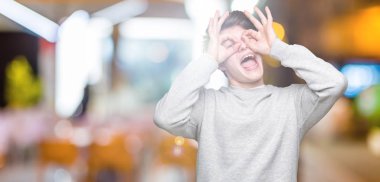 Dilini, parmaklarının arasından baktığını yapışmasını dürbün gibi ok jest yapıyor izole arka plan üzerinde sweatshirt giyen genç yakışıklı sportif adam. Deli ifade.