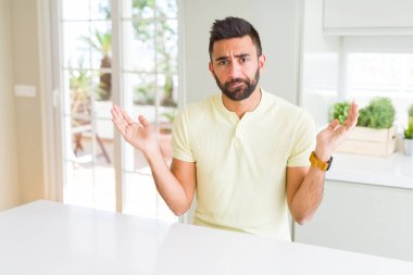 Yakışıklı İspanyol adam evde rahat sarı t-shirt silah ve elleri kaldırdı ile anlamsız ve karışık ifade. Şüphe kavramı.