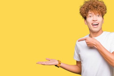 Afro saçlı genç yakışıklı adam rahat beyaz t-shirt giyen şaşırttı ve el ile sunarken kameraya gülümseyerek ve parmak ile işaret.