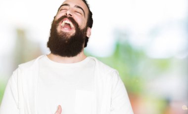 Uzun saç ve sakal sportif sweatshirt giyen genç hipster adamla gülen ve komik deli şaka çünkü yüksek sesle zor gülüyor. Mutlu ifade.
