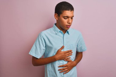 Mavi gömlek giyen genç yakışıklı arap adam mide üzerinde el ile izole pembe arka plan üzerinde duran mide, ağrılı hastalık kötü hissediyorum. Ağrı kavramı.