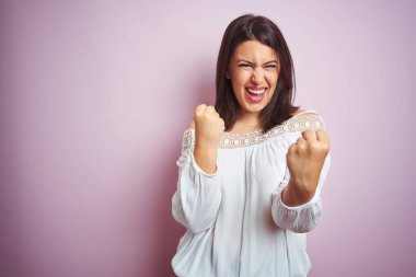 Pembe izole arka plan üzerinde genç güzel esmer kadın şaşırmış kutluyor ve kollarını kaldırdı ve açık gözleri ile başarı için hayran. Kazanan kavramı.