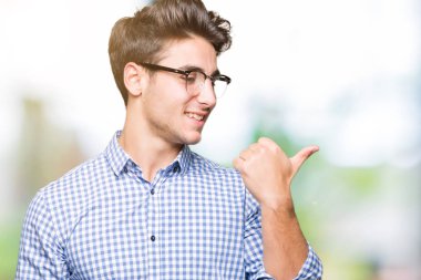 Seyir ve başparmak yanında yukarıyı mutlu yüz ile gülümseyen izole arka plan üzerinde gözlük takan genç yakışıklı adam.