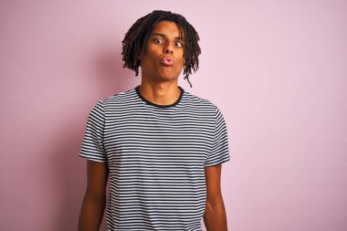 Dudaklar, çılgın ve komik jest ile balık yüz yapma izole pembe arka plan üzerinde duran lacivert çizgili t-shirt giyen dreadlocks ile Afro adam. Komik ifade.