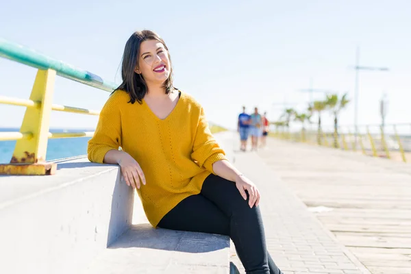 Schöne junge Frau sitzt auf einer Promenade am Meer und lächelt — Stockfoto