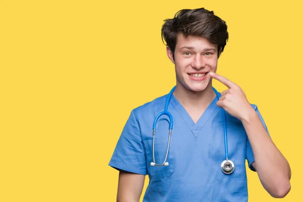 年轻医生穿着医服在孤立的背景上指着手指对脸和鼻子 微笑欢快 — 图库照片