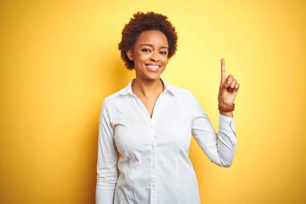 stock image African american business woman over isolated yellow background showing and pointing up with finger number one while smiling confident and happy.