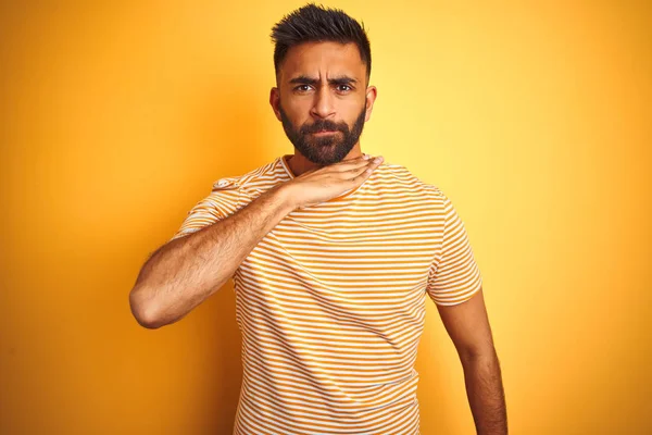 Young indian man wearing t-shirt standing over isolated yellow background cutting throat with hand as knife, threaten aggression with furious violence