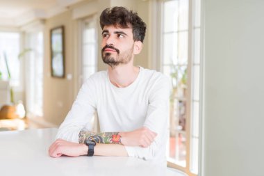 Genç giyiyor rahat gömlek beyaz uzak tarafına gülümseme ile yüzünde, doğal ifade seyir tablo oturan adam. Kendine güvenen gülüyor.