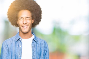 Afrikalı-Amerikalı genç afro saçlı seksi bir ifadeyle, neşeli ve mutlu yüzünü kameraya bakarak göz kırpıyor.