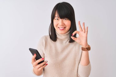 Genç güzel Çinli kadın parmakları ile ok işareti yapıyor izole beyaz arka plan üzerinde duran akıllı telefon kullanarak, mükemmel bir sembol