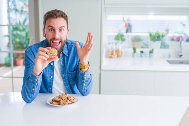 Kocaman bir gülümseme ile çığlık ve ellerini kaldırdı çerezler çok mutlu ve heyecanlı, kazanan ifade kutluyor zafer yakışıklı adam yeme çikolata cips