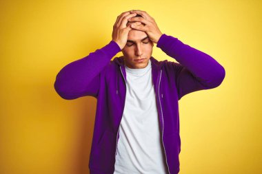 Genç yakışıklı adam sarı izole arka plan üzerinde mor sweatshirt giyen baş ağrısı umutsuz muzdarip ve stresli çünkü ağrı ve migren. Eller baş üstünde.