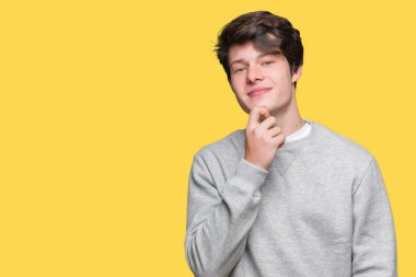 Emin çapraz kollar ve çeneme kaldırdı el ile gülümseme ile kameraya bakarak izole arka plan üzerinde sweatshirt giyen genç yakışıklı sportif adam. Pozitif düşünce.