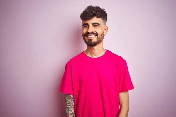 孤立したピンクの背景の上に立つタトゥーをした若者は 笑顔で横に向かって 自然な表情 自信を持って笑う — ストック写真