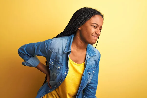 Young african american woman wearing denim shirt standing over isolated yellow background Suffering of backache, touching back with hand, muscular pain