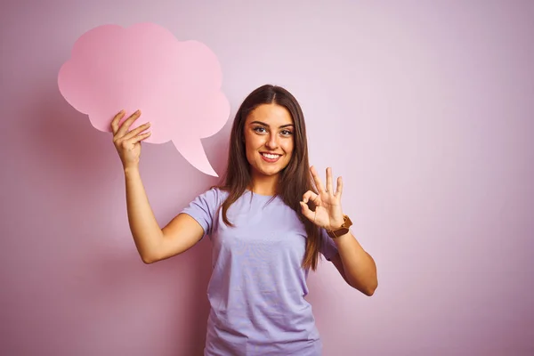 年轻的美女拿着云语音泡沫在孤立的粉红色背景做好标志用手指 优秀的符号 — 图库照片