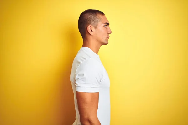 黄色の孤立した背景の上にカジュアルな白いTシャツを着た若い白人男性が横に見て 自信のある笑顔で自然な顔でプロフィールポーズをリラックス — ストック写真