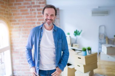 Orta yaş yaşlı adam yüzünde mutlu ve serin bir gülümseme ile karton kutular ambalaj yeni bir eve hareket. Şanslı kişi.