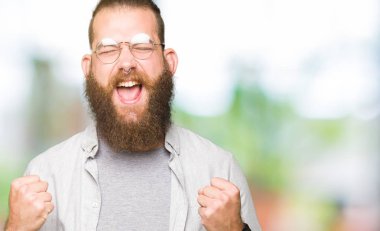 Gülümseyen ve başarı için çığlık çok mutlu ve heyecanlı kaldırdı, silah ile kazanan jest yapıyor gözlüklü genç sarışın adam. Kutlama kavramı.