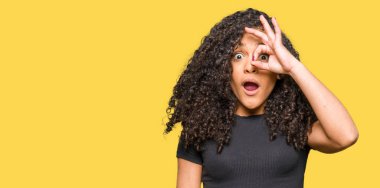 Sürpriz yüz, göz parmaklarının arasından seyir ile ok jest yapıyor kıvırcık saçlı Genç güzel kadın şok. İmansız ifade.