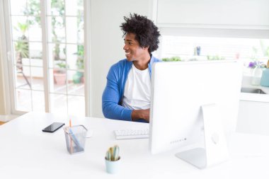 Afro-Amerikan adam bilgisayar kullanarak çalışan yüzünde gülümseme, doğal ifade ile yan bakarak. Gülmekten emin.