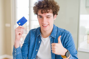 Büyük bir gülümseme ok işareti yapıyor kredi kartı mutlu tutan genç adam, parmakları ile başparmak, mükemmel işareti