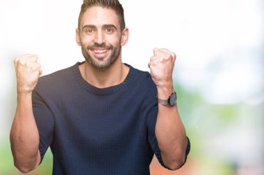 Yakışıklı delikanlı izole arka plan kutlama üzerinde kazak giyen şaşırttı ve başarı için kaldırdı kollarını açarak hayret ve gözleri açık. Kazanan kavramı.