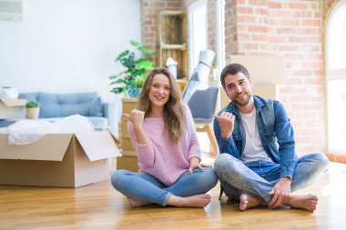 Genç güzel çift yeni bir eve mutlu yüz bakarak gülümseyerek yerde oturan hareketli ve başparmak ile yan işaret.