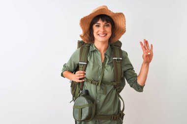 İzole beyaz arka plan üzerinde sırt çantası şapka ve su kantini giyen Yürüyüşçü kadın gösteren ve emin ve mutlu gülümserken parmakları ile işaret.