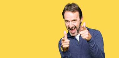 Orta yaş yakışıklı adam mutlu ve komik yüz ile kamera parmaklar işaret bir kazak giyiyor. İyi enerji ve Vibes.