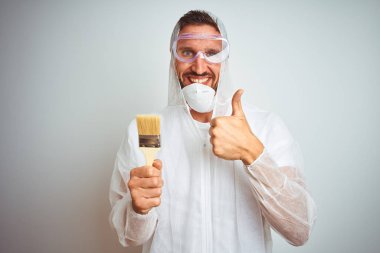 Ressam adam ok işareti yapıyor büyük bir gülümseme ile mutlu izole arka plan üzerinde fırça tutan profesyonel işçi ekipmanları giyen, parmaklarla başparmak, mükemmel işareti