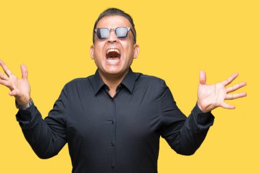 Orta yaş Arap adam üzerinde güneş gözlüğü takıyor deli kutluyor arka plan izole ve silah ile başarı için yükseltilmiş ve açık gözleri heyecanlı çığlık hayrete düşürdü. Kazanan kavramı