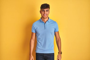 Mavi polo giyen genç hintli adam yüzünde mutlu ve serin bir gülümseme ile izole sarı arka plan üzerinde duruyor. Şanslı kişi.