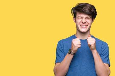 Zafer kutluyor gülümseyen izole arka kolları olan başarı için heyecan üzerinde mavi t-shirt giyen genç yakışıklı adam kaldırdı. Kazanan kavramı.