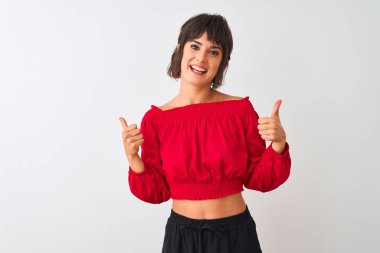 Kırmızı yazlık t-shirt giyen genç güzel kadın izole beyaz arka plan başarı işareti el ile olumlu jest yapıyor ayakta, gülümseyen ve mutlu başparmak kadar. Neşeli ifade ve kazanan jest.