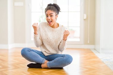 Afro saç ile güzel genç Afrikalı Amerikalı kadın yerde oturan sürpriz kutluyor ve silah ile başarı için hayran kaldırdı ve açık gözler. Kazanan kavramı.