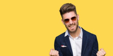 Güneş gözlüğü ve moda Blazer giyen genç yakışıklı zarif adam çok mutlu ve heyecanlı silah ile kazanan jest yaparak, gülümseyen ve başarı için çığlık kaldırdı. Kutlama konsepti.