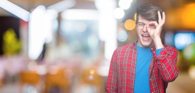 Genç yakışıklı öğrenci adam izole arka plan üzerinde gözlük takan el gülümseyerek ok jest yapıyor, mutlu yüz ile parmaklardan bakan göz.