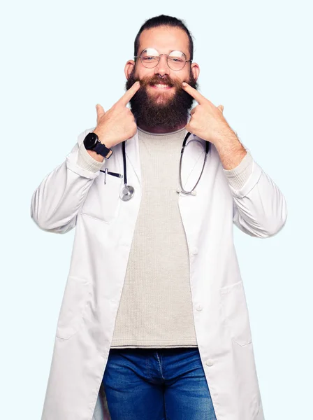 ひげ医療身に着けている若いブロンド医師男は口を開けて笑顔をコート 指を指すし 陽気な笑顔 — ストック写真