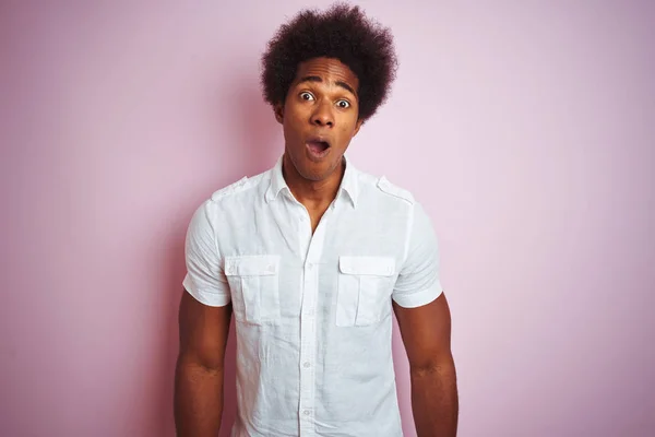 Young american man with afro hair wearing white shirt standing over isolated pink background afraid and shocked with surprise expression, fear and excited face.